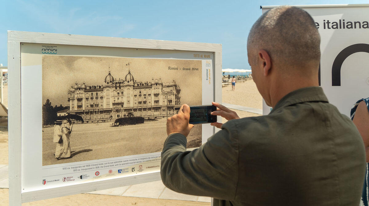 Una mostra di fotografia in spiaggia tra i bagni 47-100, per rivivere la vacanza a Rimini dall'ottocento a oggi - Il sindaco fotografa con lo smartphone una delle foto della mostra