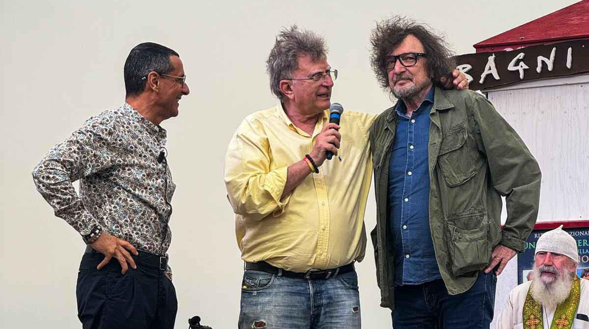Red Ronnie in spiaggia per un evento di pace, tra gli spettatori spunta anche Cecchetto - Red Ronnie con Claudio Cecchetto